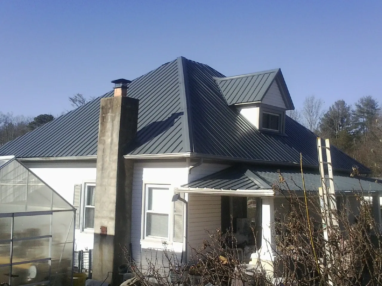 Dark blue standing seam metal roof on a white farmhouse with dormer — Slate & Tile Roof Repair by Roofing Brothers in Chepachet