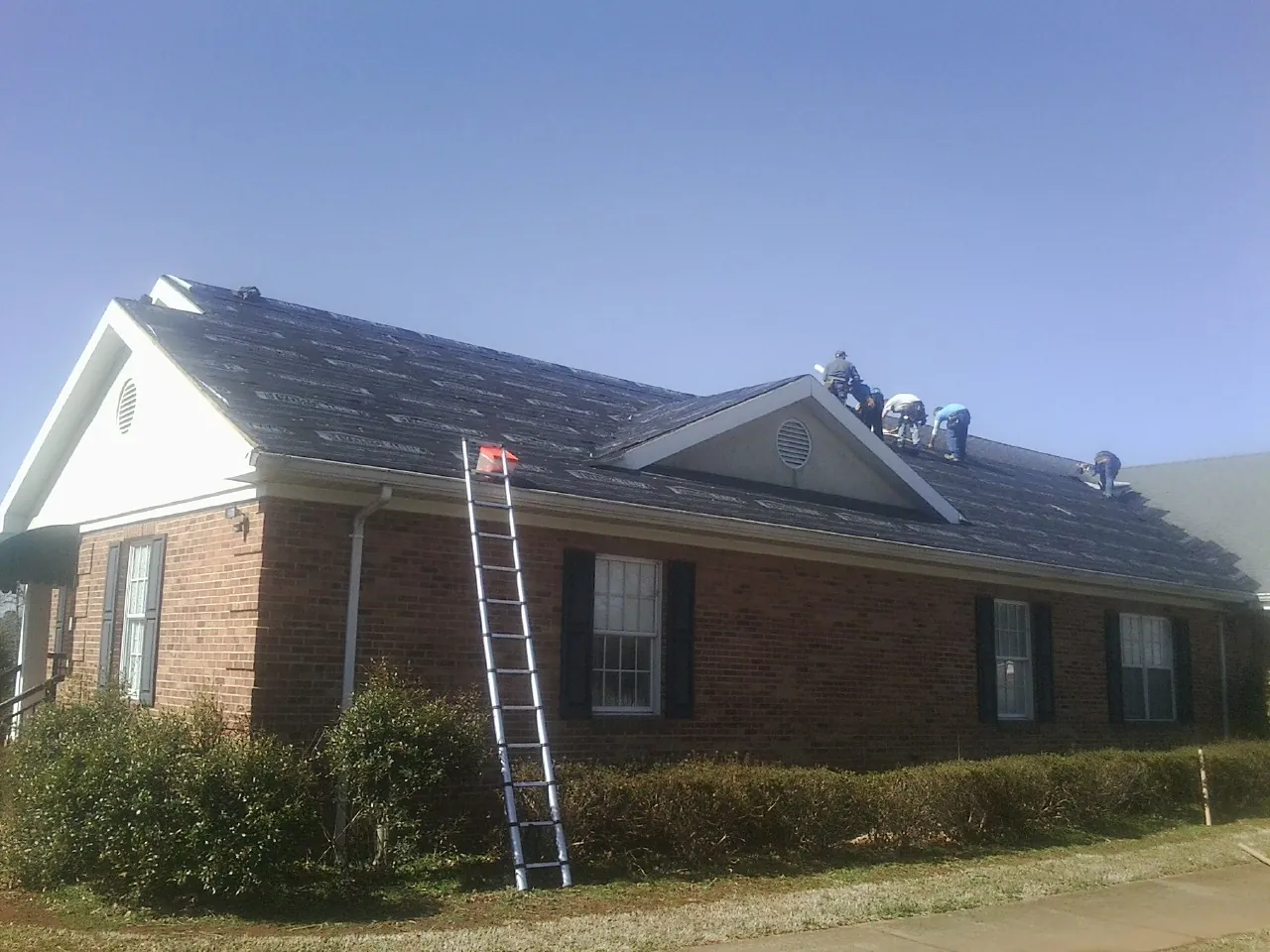 Crew tearing shingles off a brick ranch roof with a ladder set — Metal Roof Repair work by our crew in Chepachet