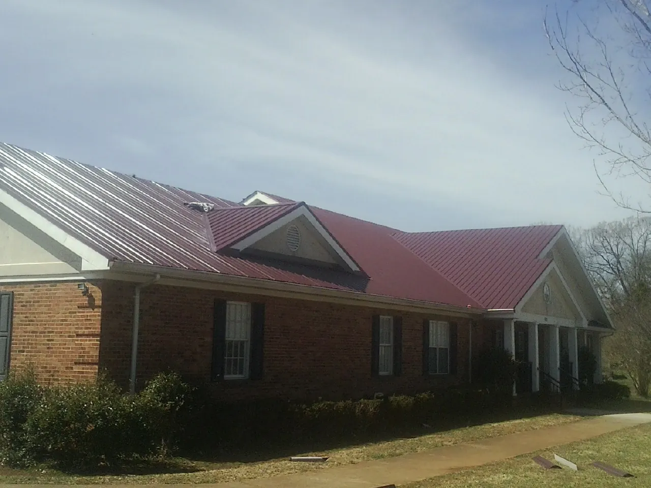 Red metal roof with gabled entries on a long brick building, from a Hail Damage Roof Repair job in Chepachet