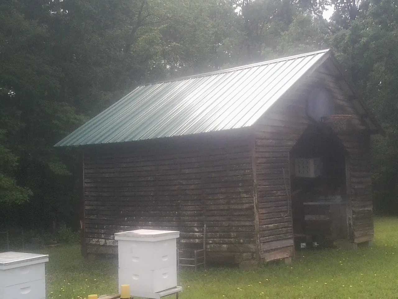 Green metal roof on a weathered barn beside stacked beehives in Chepachet