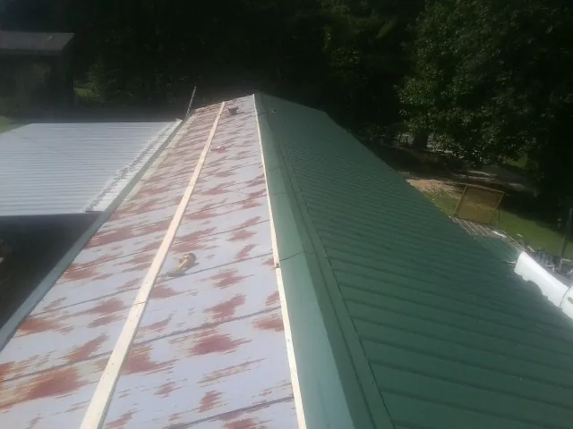 Old rusted panels beside newly installed green metal roofing — Wind Damage Roof Repair by Roofing Brothers in Chepachet