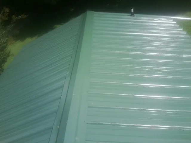 New green metal panels meeting at the ridge of a roof — Flat Roof Repair work by our crew in Chepachet