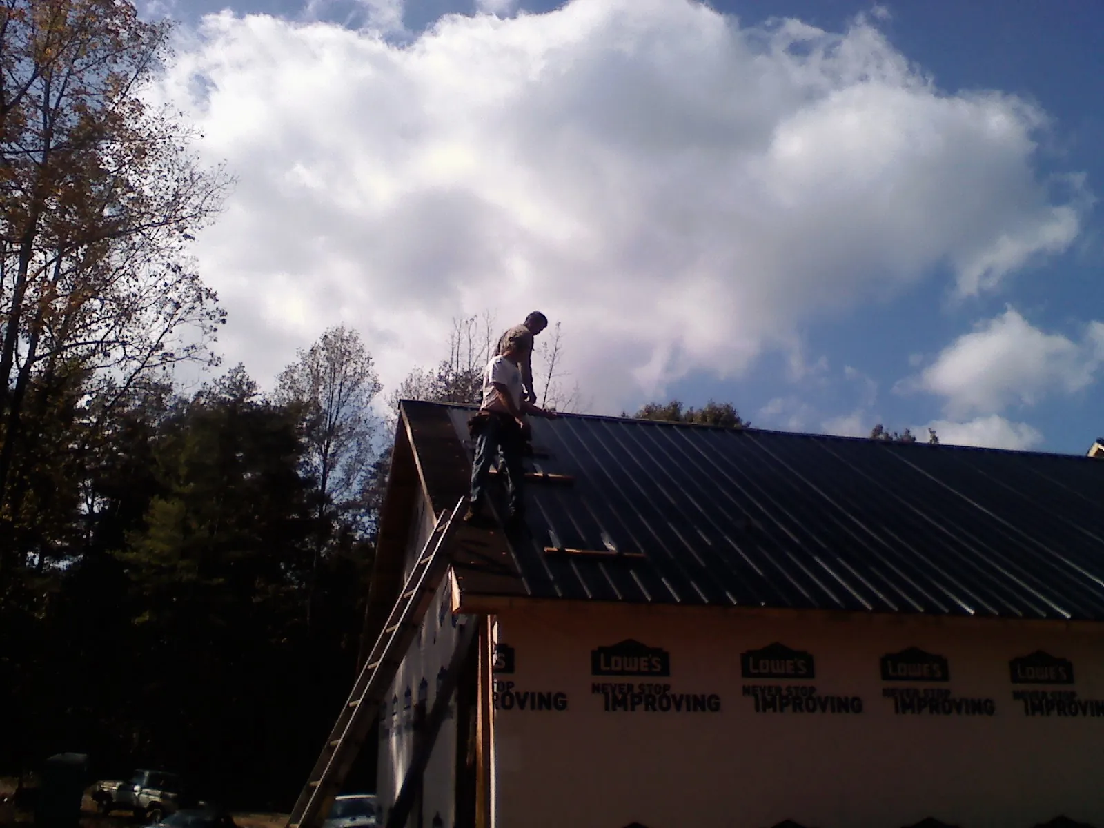 Roofer fastening dark metal panels high against a cloudy sky, from a Roof Inspection job in Chepachet