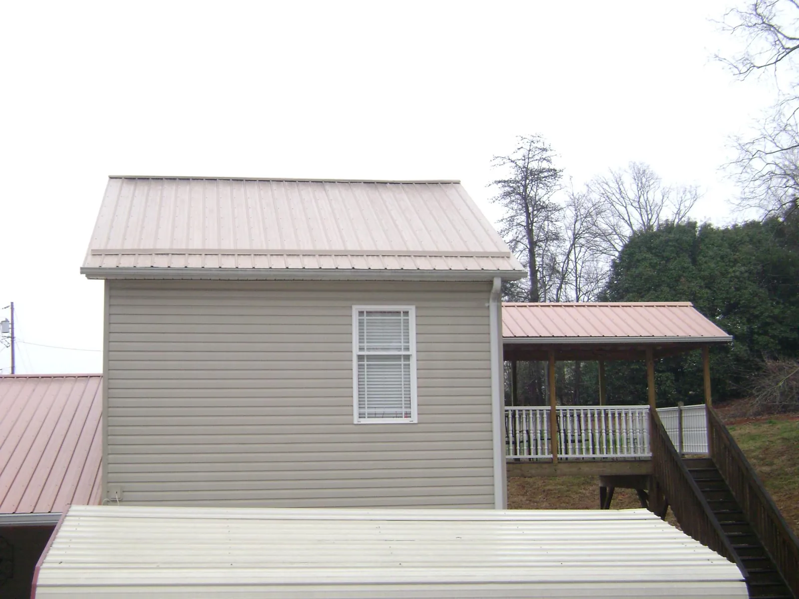 Tan metal roofs on a two story addition and attached porch, from a Roof Replacement job in Chepachet